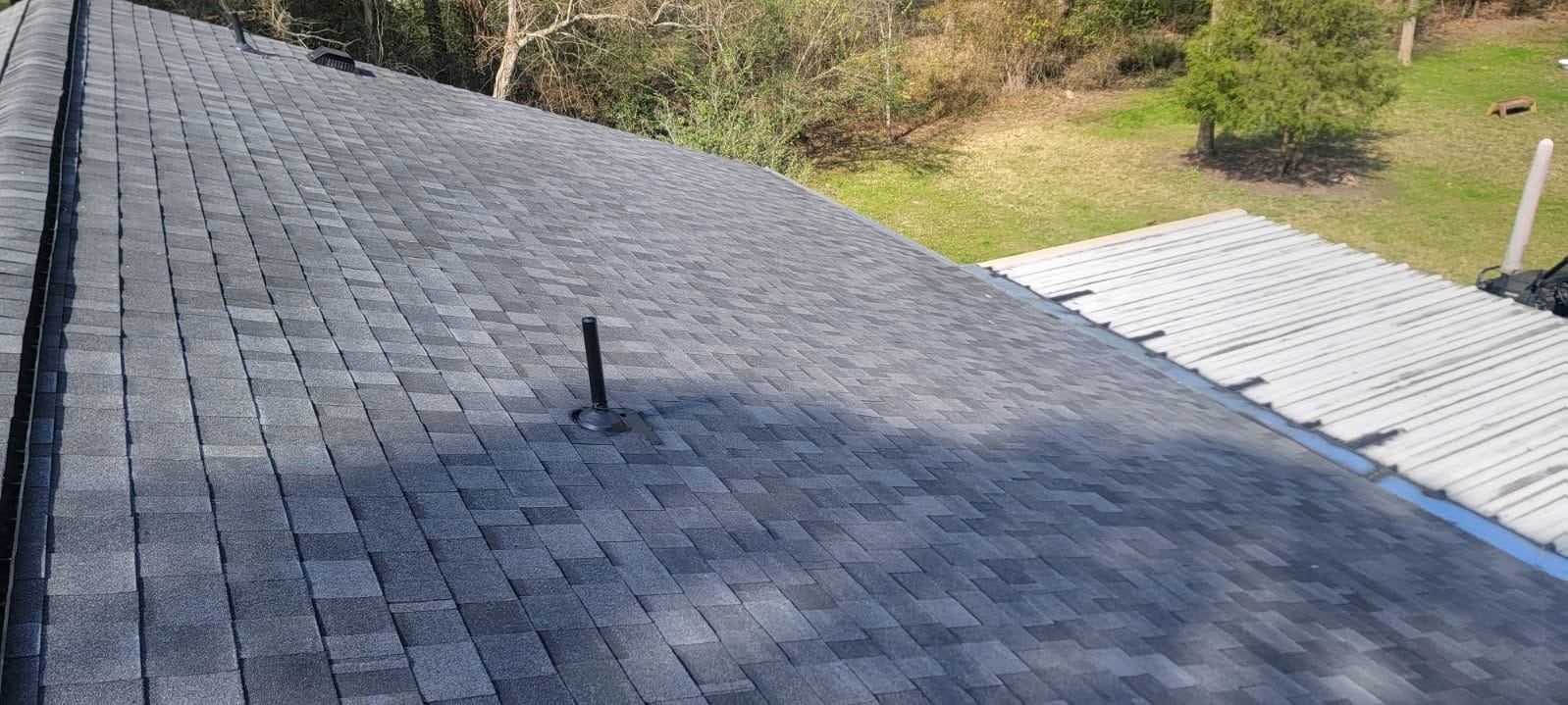 Newly installed charcoal architectural shingles with fresh ridge cap and sealed vent flashings after replacement