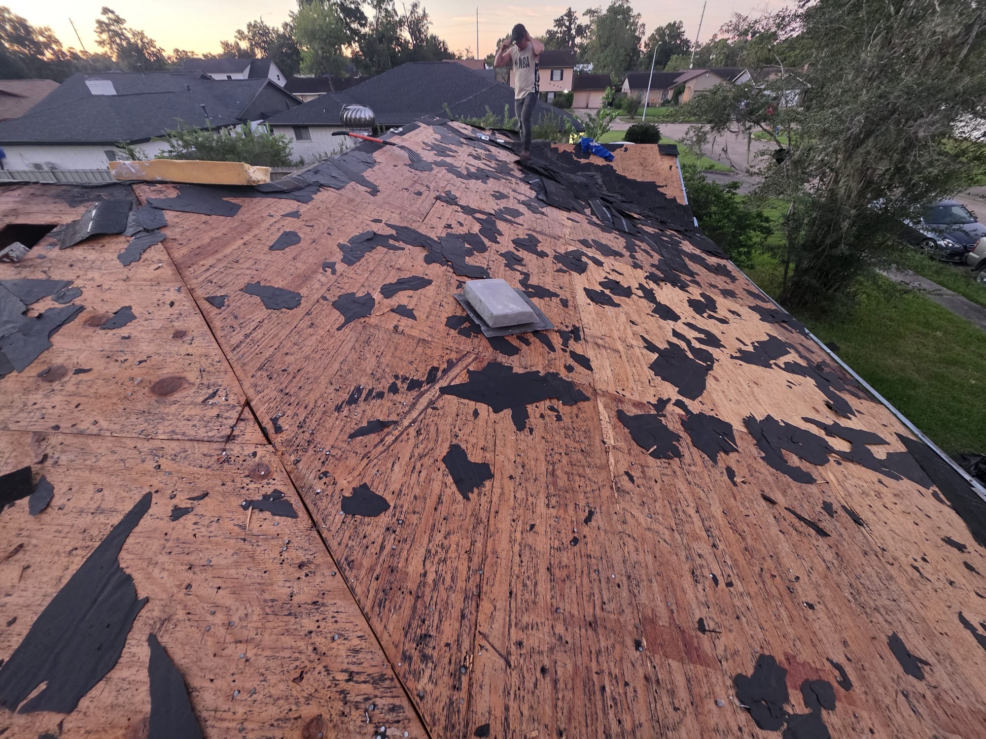 Old shingles stripped away, leaving bare decking and torn underlayment before replacement